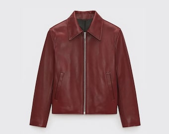 May include: A burgundy leather jacket with a collared neckline and a silver zip. The jacket has long sleeves and two front pockets. The jacket is a solid colour and has a classic design.