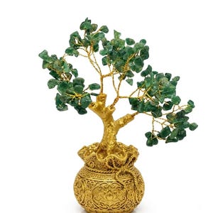 Puede incluir: Una escultura de árbol decorativa con numerosas piedras verdes pequeñas y pulidas unidas a ramas de alambre fino y flexible de color dorado. El árbol está anclado en una base redonda de color dorado con texturas y relieves.