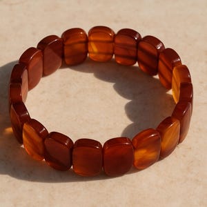 May include: A stretch bracelet featuring rectangular amber-colored beads. The bracelet's warm tones range from deep brown to golden yellow, creating a striking contrast. This jewelry piece is designed to be worn around the wrist.