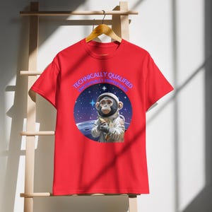 May include: Red t-shirt with a cartoon monkey astronaut design. The image includes the text "Technically Qualified Emotionally Unprepared" in a circular design. The monkey is holding a banana in a space scene.