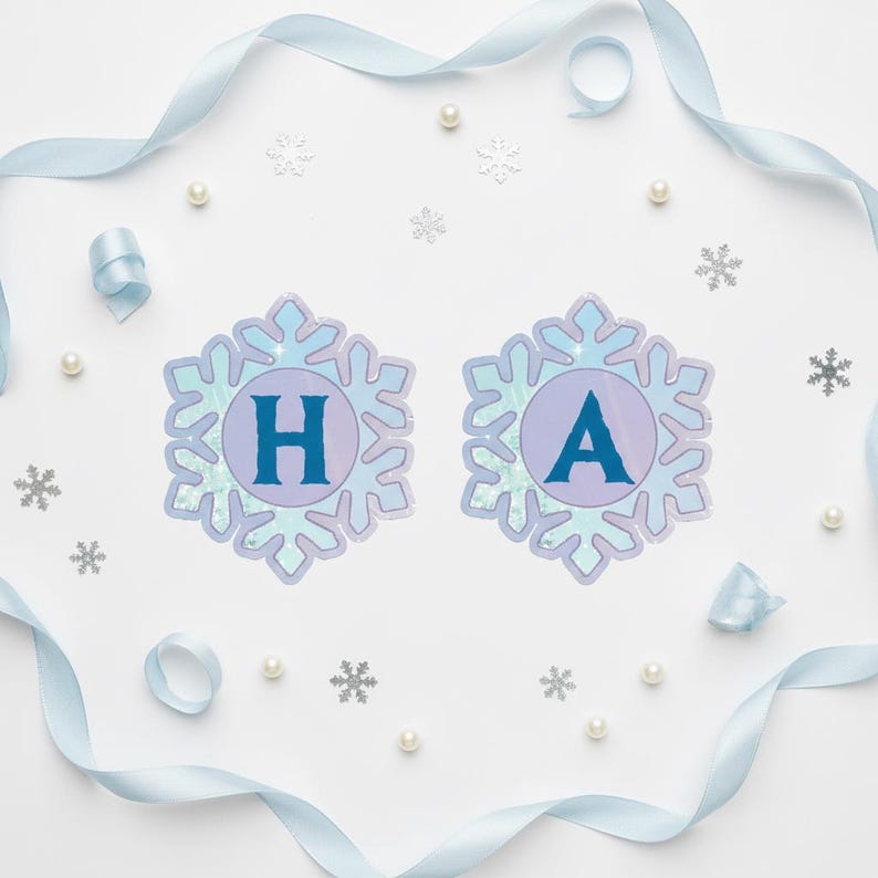 Op de afbeelding: Een feestelijke banner met de letters "HA" in blauwe letters, elk in een sneeuwvlokvormig ontwerp. De banner is omgeven door lichtblauw lint, imitatieparels en sneeuwvlokconfetti op een witte achtergrond.