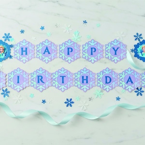Op de afbeelding: Een 'Happy Birthday'-banner met sneeuwvlokvormige letters in blauw en paars. De banner bevat afbeeldingen van een prinses en is versierd met blauwe en witte sneeuwvlokken en een lichtblauw lint. Perfect voor een themaverjaardagsfeest.