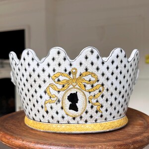 May include: White ceramic bowl with a scalloped rim and a diamond pattern. The bowl features a gold bow and a black silhouette of a person in a cameo. The base has a gold trim.