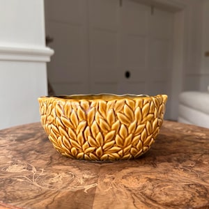 Peut inclure: Un bol décoratif en céramique avec un motif de feuilles dans les tons marron et or. Le bol a un bord festonné et repose sur une table en bois. Le bol est probablement utilisé à des fins décoratives.