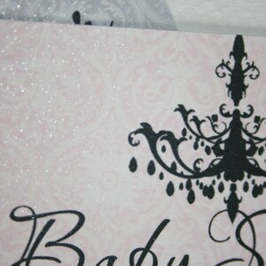 Peut inclure: Invitation de baby shower rose et blanche avec un motif de lustre noir. Le texte "Baby Shower" est &eacute;crit en script &eacute;l&eacute;gant. Le fond pr&eacute;sente un motif floral subtil et des accents de paillettes.
