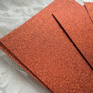 May include: A stack of orange glitter cardstock paper. The paper has a fine glitter texture.