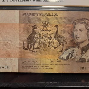 May include: An Australian one-dollar banknote with a portrait of a woman, the word "AUSTRALIA", and the number "1". The note shows a kangaroo and an emu with a coat of arms.