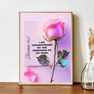 May include: A framed print featuring a pink rose with a stem and leaves. The print has the text "Romans 12:2" and "I AM TRANSFORMED BY THE RENEWING OF MY MIND." The background is a gradient of pink and purple.