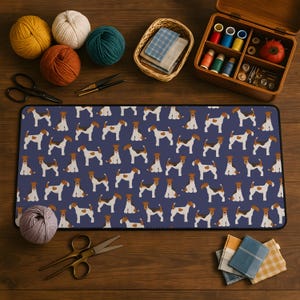 May include: A navy blue rectangular desk mat featuring a repeating pattern of brown and white terrier dogs. The mat is surrounded by sewing supplies, including spools of thread, scissors, and yarn.
