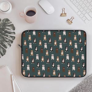 May include: A black laptop sleeve featuring a repeating pattern of various dog breeds in brown, black, and white against a dark teal background. The sleeve has a black zipper closure.