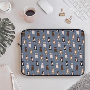 May include: A laptop sleeve with a repeating pattern of various dog breeds in brown, black, and white on a blue background. The sleeve is rectangular with a black zipper. The design includes a variety of dog breeds.