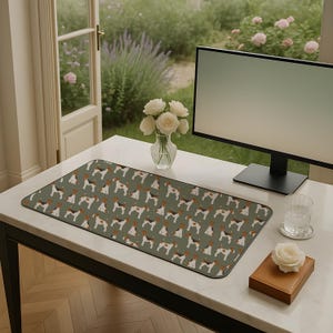 May include: A rectangular desk mat with a repeating dog pattern on a muted green background. The mat is on a white desk, with a computer monitor, a vase of white roses, and a glass of water. The mat measures approximately 70 cm in length.