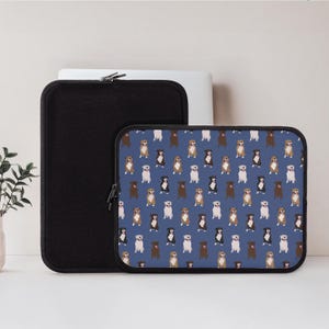 May include: A black laptop sleeve and a blue laptop sleeve with a repeating pattern of various dog breeds. The dogs are in shades of brown, black, and white. The sleeves are zippered and sit on a white surface.