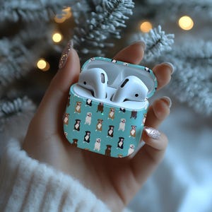 May include: A light blue protective case for wireless earbuds featuring a repeating pattern of various dog breeds in brown, black, and white. The case is open, revealing two white wireless earbuds inside, and the exterior surface is smooth.