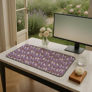 May include: A rectangular desk mat featuring a repeating pattern of dogs in brown, black, and white on a lilac background. The mat is on a white desk with a computer monitor, a vase of white roses, and a glass of water.