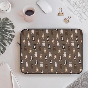 May include: A brown laptop sleeve featuring a repeating pattern of various dog breeds in different colors. The dogs are depicted in a standing pose against a brown background. The sleeve has a black zipper.