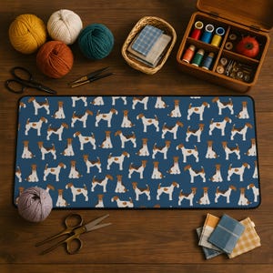 May include: A blue desk mat with a repeating pattern of brown and white dogs. The mat is surrounded by sewing supplies, including yarn, scissors, and a wooden box with spools of thread and needles.