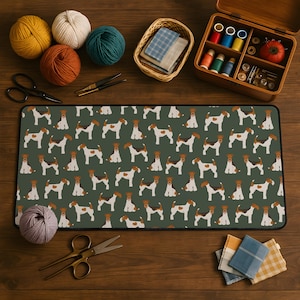 May include: A green desk mat featuring a repeating pattern of brown and white dogs. The mat is surrounded by sewing supplies, including spools of thread, scissors, and yarn in various colors. A wooden sewing box is also present.