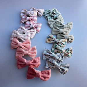 Puede incluir: Una colección de accesorios para el cabello con lazos de tela en varios colores y patrones. Los lazos incluyen tonos de rosa, rojo, verde y estampados florales. Los lazos están dispuestos en forma circular.