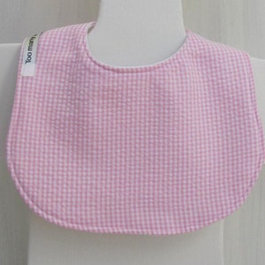 May include: Pink and white gingham baby bib with a white label that says "Too many" on it.