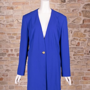 Può includere: Un blazer blu reale vibrante caratterizzato da un profondo scollo a V, maniche lunghe e un unico bottone decorativo color oro al centro. Il capo presenta una silhouette strutturata con spalline e una finitura in tessuto liscio e tinta unita.