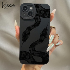Puede incluir: Funda de teléfono negra con un diseño detallado de dos serpientes. La funda tiene un acabado mate y el texto "Venom Case" es visible. La funda está diseñada para un teléfono con una cámara de triple lente. Las serpientes son de color gris oscuro.