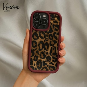 May include: A burgundy-framed phone case with a leopard print design. The case features a gold and brown spotted pattern and the text "Venom Case" in the upper left corner.
