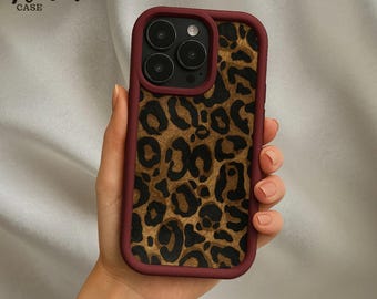 May include: A burgundy-framed phone case with a leopard print design. The case features a gold and brown spotted pattern and the text "Venom Case" in the upper left corner.