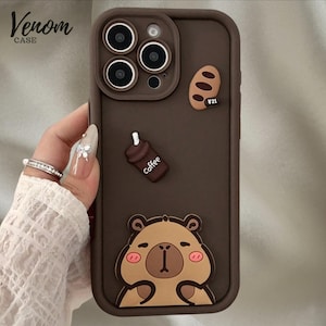 Könnte beinhalten: Braune Handyhülle mit Bär, Kaffeetasse und Brot-Design. Der Schriftzug "Venom Case" befindet sich oben links. Die Hülle ist für ein Telefon mit drei Kameralinsen konzipiert.