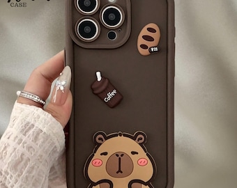 May include: A brown phone case with a bear, coffee cup, and bread design. The case has the text "Venom Case" in the upper left corner. The case is designed for a phone with three camera lenses.