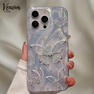 May include: Iridescent phone case with embossed butterfly motifs and star details. The case features the text "Venom CASE". The case is designed to fit a smartphone.