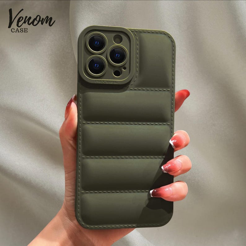 Pode incluir: Capa de telefone verde-oliva com design acolchoado. A capa tem uma prote&ccedil;&atilde;o de lente de c&acirc;mera elevada e o texto "Venom CASE" no canto superior esquerdo. A capa &eacute; projetada para um smartphone.