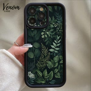 May include: A dark green phone case with a botanical design featuring various shades of green leaves and white flowers. The case has a black border and the text "Venom Case" in the upper left corner.