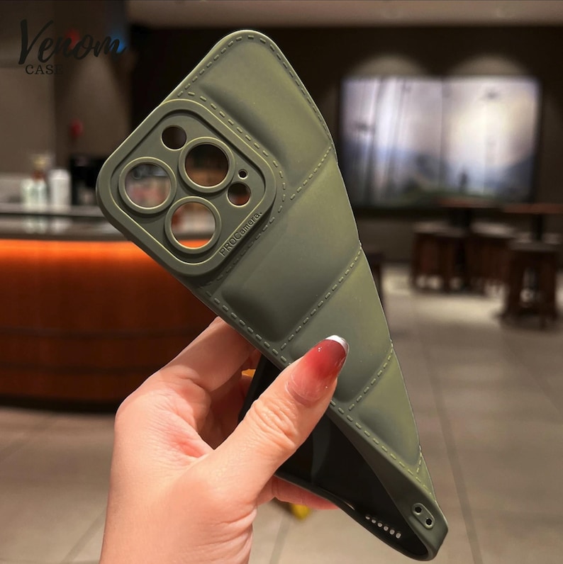 Pode incluir: Capa de telefone verde-oliva com design acolchoado. A capa tem uma se&ccedil;&atilde;o elevada para a c&acirc;mera com o texto "PRO Camera". A marca "Venom Case" &eacute; vis&iacute;vel no canto superior esquerdo.