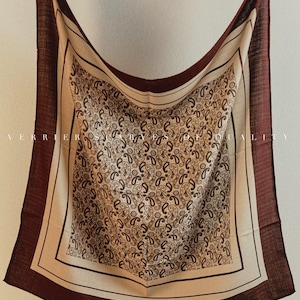 Könnte beinhalten: Ein quadratischer Schal mit einem Paisley-Muster in Braun-, Beige- und Cremetönen. Der Schal hat einen dunkelbraunen Rand und wird von Holzklemmen gehalten. Der Text "VERRIER ROSES OF QUALITY" ist auf dem Schal aufgedruckt.
