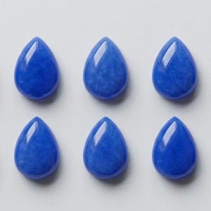 Peut inclure: Dix cabochons en forme de goutte d'eau d'un bleu royal éclatant. Chaque pièce présente une surface lisse et polie avec un sommet arrondi et une base plate, disposées en deux rangées horizontales de cinq articles identiques sur un fond neutre.
