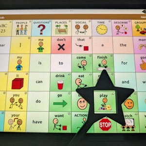 May include: A digital tablet screen displaying an augmentative and alternative communication grid with various colorful icons, text labels, and categories. A black star-shaped pointer is positioned over the icon labeled play, which depicts a figure.