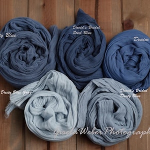 May include: Four rolls of blue fabric in different shades of blue, including dusty blue, steel blue, denim blue, and dusty blue gray. The fabric is arranged in a circle on a wooden surface. The text "David's Bridal" and "Gisela Weber Photography" is visible in the image.