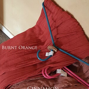 May include: Two pieces of fabric, one burnt orange and one cinnamon, are draped over a blue hanger. The fabric is folded and has a textured look.