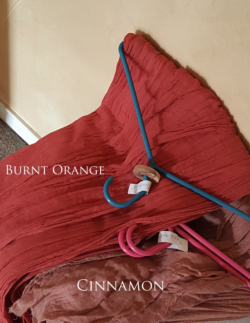 May include: Two pieces of fabric, one burnt orange and one cinnamon, are draped over a blue hanger. The fabric is folded and has a textured look.