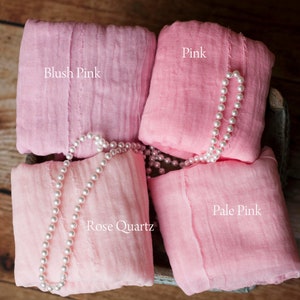 May include: Four squares of pink fabric, labeled "Blush Pink", "Pink", "Rose Quartz", and "Pale Pink". A strand of white pearls is draped over the fabric squares.