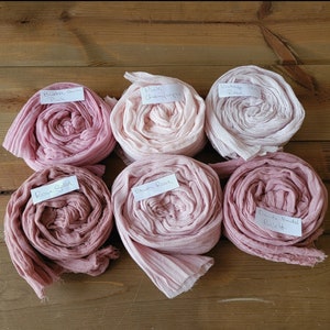 May include: Six spools of pink fabric dyed in different shades of pink. The fabric is rolled up and labeled with the names of the colors: "Bubble Gum Pink", "Pink Champagne", "Vintage Tea Rose", "Rose Petal", "Blush Rose", and "David's Bridal Ballet".