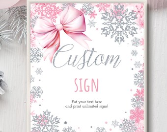 May include: A framed sign with a pink bow and snowflake design. The sign has the words "Custom SIGN" in silver script. The sign is surrounded by pink and silver snowflakes, with text at the bottom.