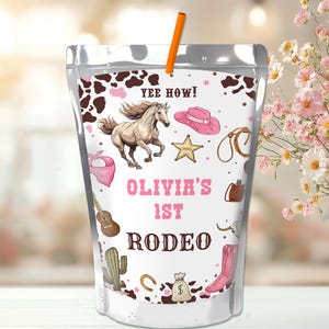 May include: A clear, resealable pouch with an orange straw, featuring a rodeo-themed design. The design includes a running horse, cowboy hat, and the text "Olivia's 1st Rodeo". The pouch has a brown and pink color scheme.