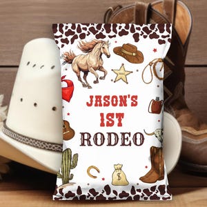 May include: A rectangular snack bag with a white background and brown cow print borders. The bag features illustrations of a horse, cowboy hat, sheriff star, lasso, cactus, money bag, and boots. The text reads JASON'S 1ST RODEO in red and brown.