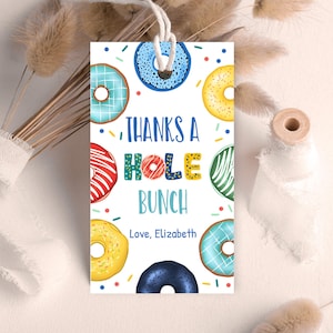 May include: A rectangular gift tag featuring colorful donuts and the text "THANKS A HOLE BUNCH". The donuts are in various colors, including blue, yellow, red, and green, with sprinkles. The tag is tied with a white string and includes the text "Love, Elizabeth".