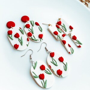 May include: A set of three pairs of handmade polymer clay earrings featuring red and green tulip designs. The earrings are oval and rectangular shaped.