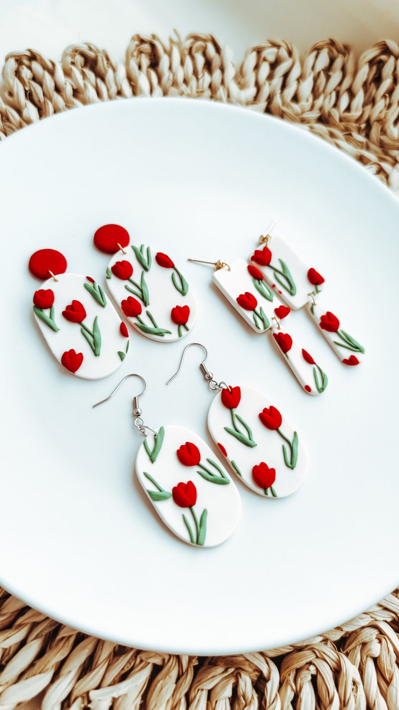 May include: A set of three pairs of handmade polymer clay earrings featuring red and green tulip designs. The earrings are oval and rectangular shaped.