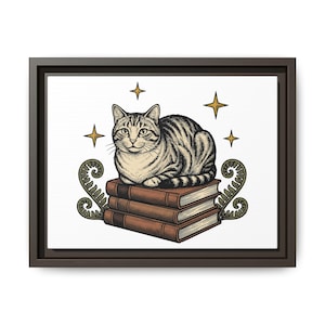 May include: A framed wall art print featuring a tabby cat resting on a stack of three brown books. The illustration includes four gold-colored four-pointed stars and two green fern-like fronds on either side of the books, all on a white background.