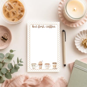 May include: A rectangular notepad with a white background and a tan polka dot border. The text "but first, coffee" is printed at the top. The bottom features four illustrated coffee cups with smiling faces, including mugs and a lidded cup.